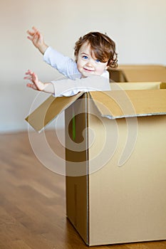 Toddler baby girl sitting inside brown cardboard box.
