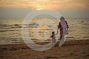 toddler baby girl walking with her mother on sea beach at sunset