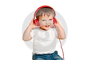 Toddler baby listens to music in red headphones on a studio isolated o