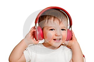 Toddler baby listens to music in red headphones on a studio isolated on a white background. Happy child in a blue jeans listens to