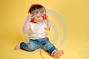 Toddler baby listens to music in red headphones on a studio yellow ba