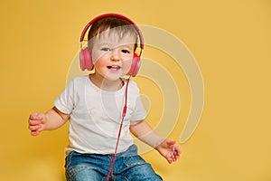 Toddler baby listens to music in red headphones on a studio yellow ba