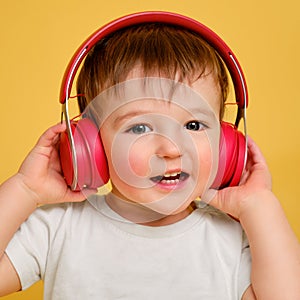 Toddler baby listens to music in red headphones on a studio yellow ba
