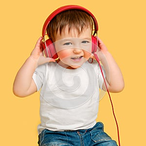 Toddler baby listens to music in red headphones on a studio yellow ba