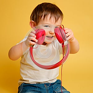 Toddler baby listens to music in red headphones on a studio yellow ba