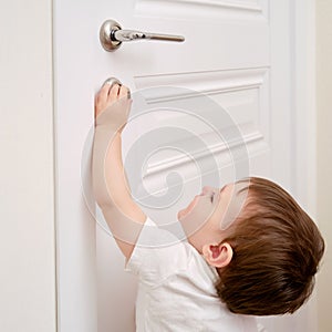 Toddler baby opens the lock, child hand close-up. White wooden door,