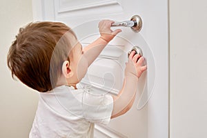 Toddler baby opens the lock, holding the door handle, child hand close-