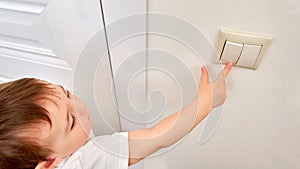 Toddler baby reaches for the light switch, child's hand turns on the lam
