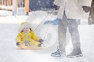 Toddler baby rides in the snow on icesled, a winter playground. Mother