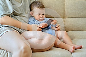 Toddler baby sits with his mother and looks into the phone. Mom and c