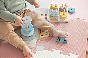 Toddler baby sitting on carpet playing with colorful wooden stacking toy