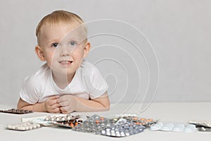 Toddler baby on a white background with pills and medicines