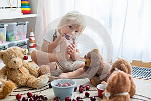 Toddler blond child, cute boy, eating cherries with teddy bears
