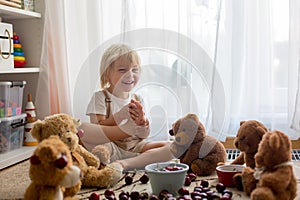 Toddler blond child, cute boy, eating cherries with teddy bears