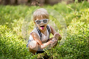 Toddler blond child, eating wild blueberries in forest