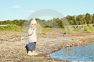 Toddler boy in autumn clothes eating bread by water