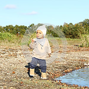 Toddler boy in autumn clothes eating bread by water