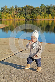 Toddler boy in autumn clothes eating bread by water