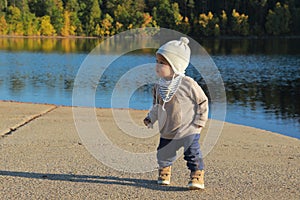 Toddler boy in autumn clothes eating bread by water