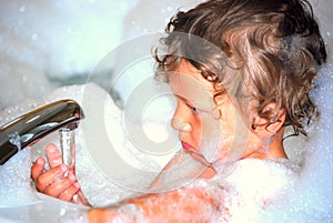 Toddler boy in bubble bath playing with faucet