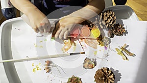 Toddler boy is painting yellow leaves and pine cones in fall with eco friendly paint. Sensorial activity at home photo