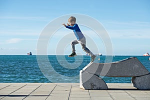 Toddler boy jumping from a stone sculpture by the sea photo