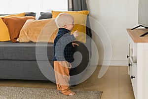Toddler boy laughing having fun standing near sofa in living room at home copy space. Adorable baby making first steps