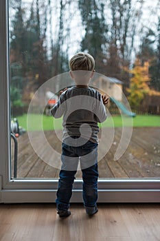 Toddler boy looking outside the window on a rainy day