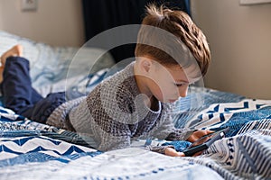 Toddler boy is lying looking at the phone. The concept of dependence on gadgets