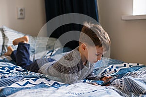 Toddler boy is lying looking at the phone. The concept of dependence on gadgets