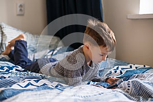 Toddler boy is lying looking at the phone. The concept of dependence on gadgets