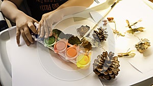 Toddler boy is painting yellow leaves and pine cones in fall with eco friendly paint. Sensorial activity at home photo