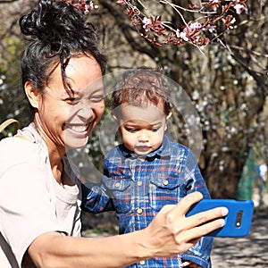 Toddler boy with Papuan mom taking selfie by bush with pink blossoms