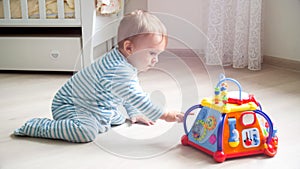 Adorable toddler boy playing with electronic toy on floor at living room