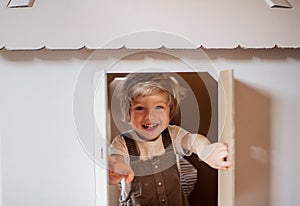 A toddler boy playing indoors with cardboard house at home.