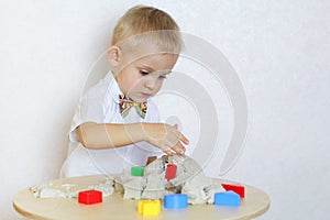 A toddler boy playing with kinetic sand, a great activity to develop fine motor skills