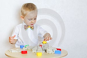 A toddler boy playing with kinetic sand, a great activity to develop fine motor skills