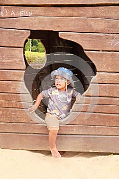 Toddler boy playing on playground - climbing out from hole of boat