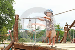 Toddler boy playing on playground - standing on bridge