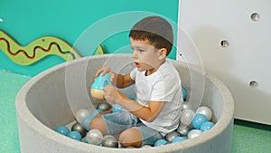 Toddler boy playing with a toy while sitting in a ball pit full of colorful balls. A ball pit - a great place for kids
