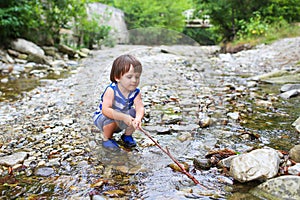 Toddler boy plays with stick in flashy river