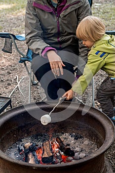 Toddler boy roasting large marshmallow on a stick over the campfire firepit. Camping family fun