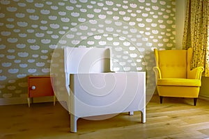 Toddler boy`s sleeping room, with cloud pattern on wall, vintage chair, wooden floor and orange bedside table