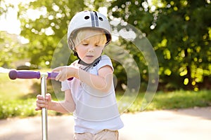 Toddler boy in safety helmet learning to ride scooter