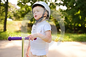 Toddler boy in safety helmet learning to ride scooter