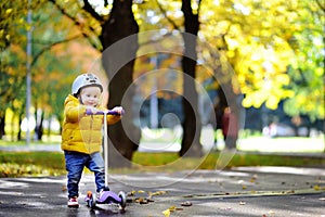 Toddler boy in safety helmet learning to ride scooter