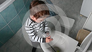 Toddler boy shows how he washes the toilet with a liquid soap.