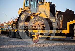 Toddler boy sits with his back and with interest examines the huge yellow caterpillar bulldozer