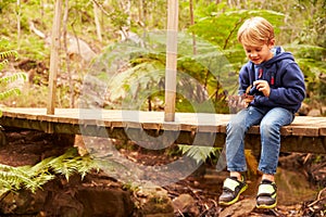 Toddler boy sitting alone on a wooden bridge in a forest