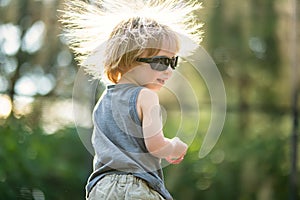 Toddler boy with sunglasses and messy hair jumping on a trampoline in a backyard. Sports and exercises for children. Summer